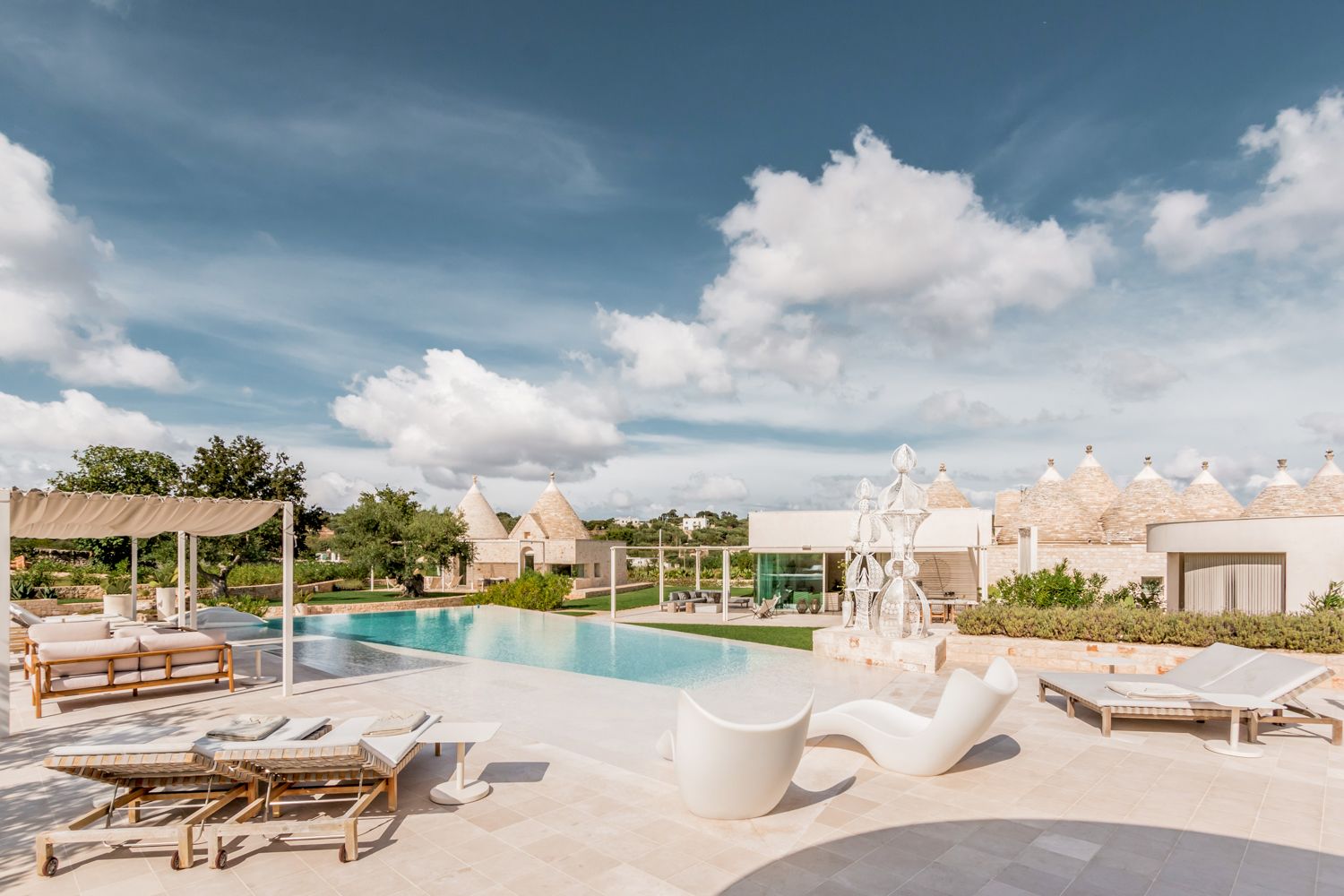 Trullo Barbagianni infinity pool with white loungers and trulli views, Cisternino, Puglia, Italy